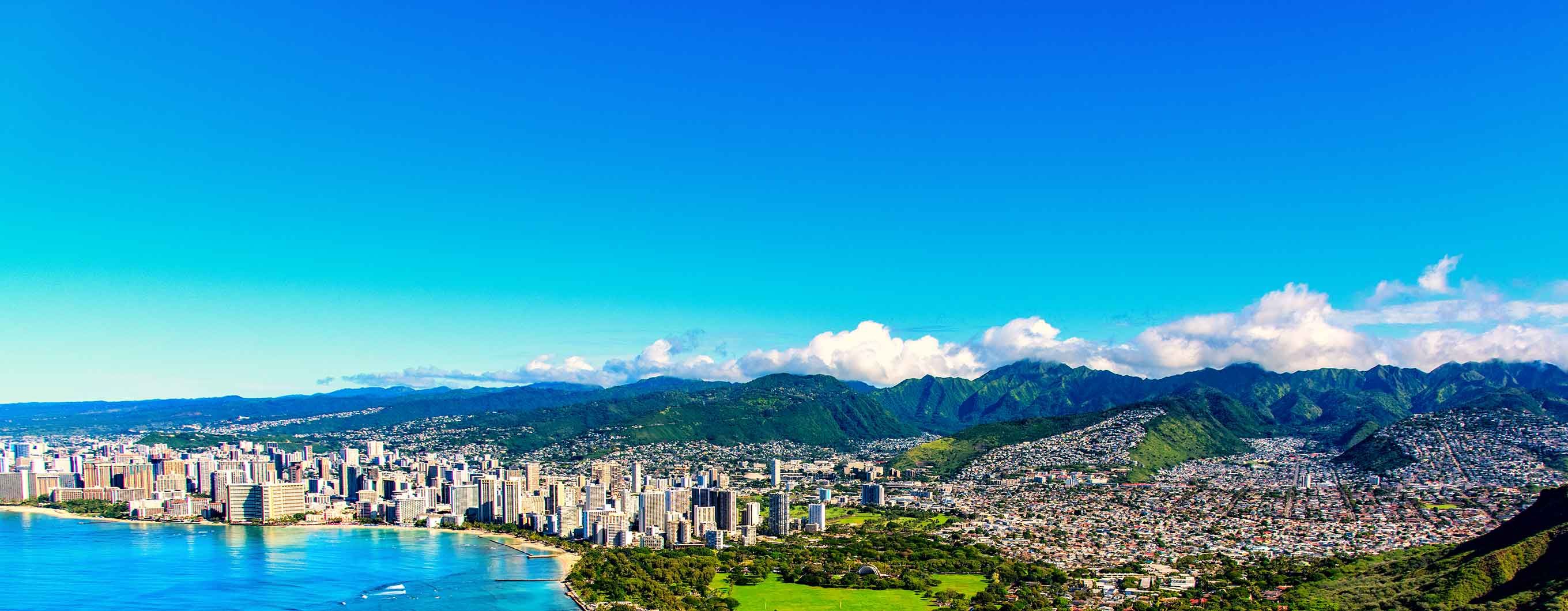 The ocean coastline in Hawaii with buildings, trees, mountains and the beach