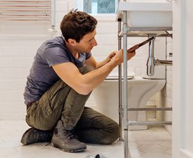 man kneeling at a bathroom sink working on the pipes
