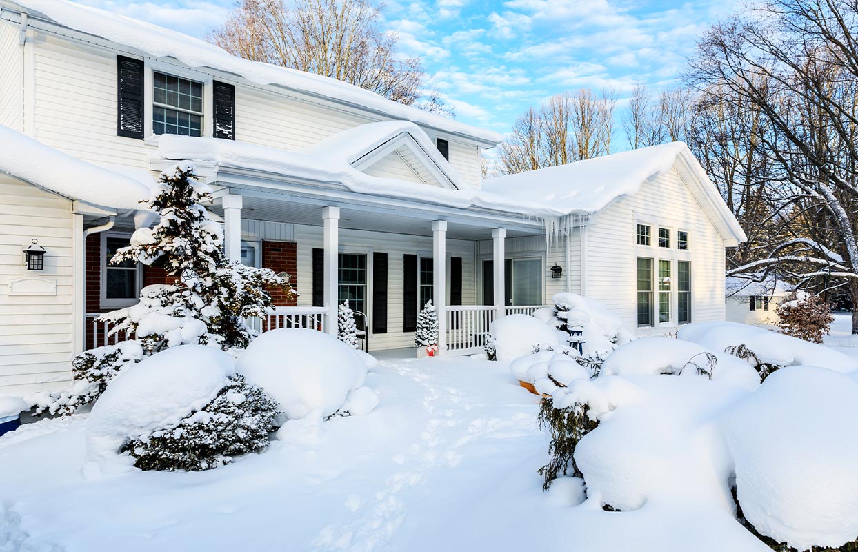 sideview of a white home with snow on the roof and around the home