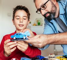 A father and son playing with a toy car in a kids room