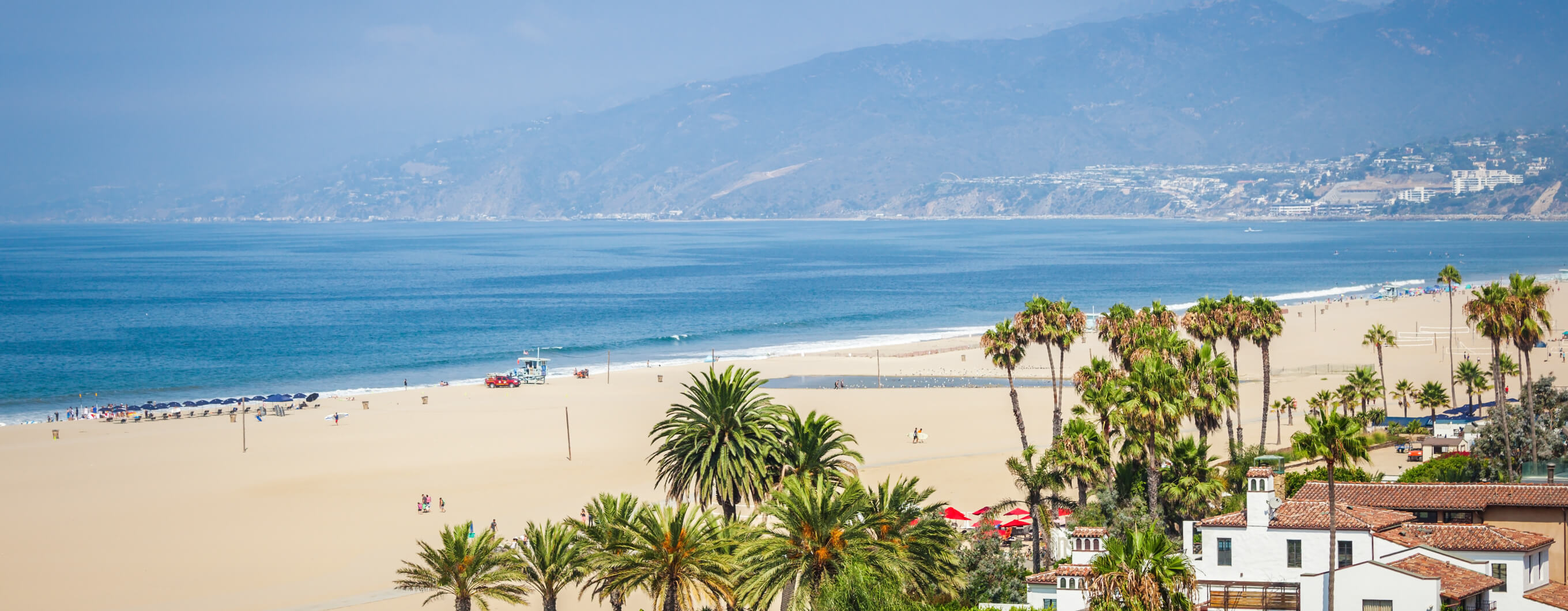 Blue sky and beach, with houses and palm trees on the right side of the frame.