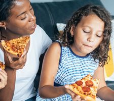 A mother and her two kids eating pizza on a couch