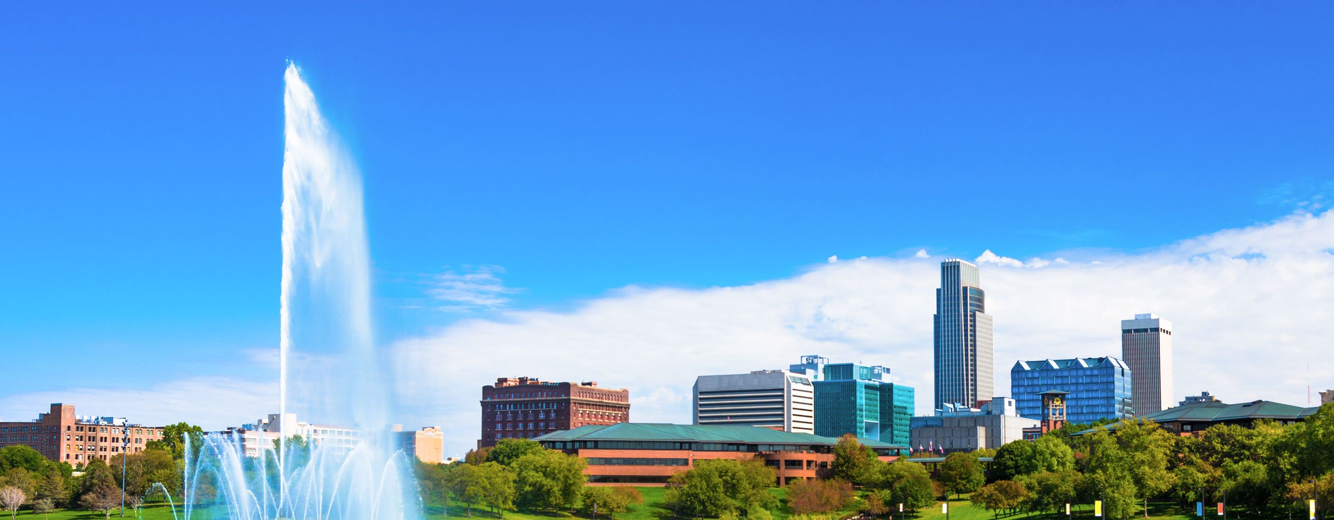 Image of a city with a pond nearby, a water feature in the pond is shooting water into the sky