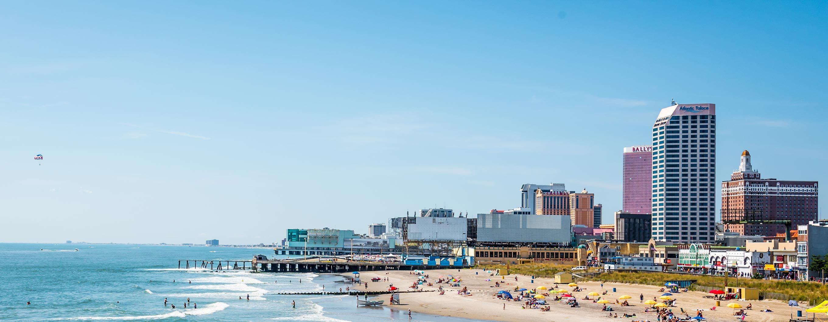 Image of a New Jersey beach with people on it, a boardwalk and buildings in the background