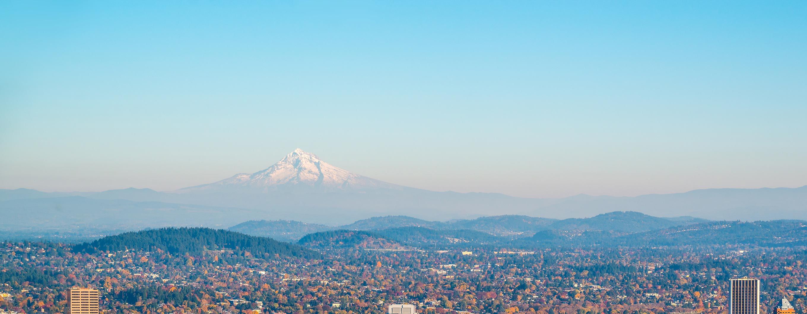 Zoomed-out image of a city with rolling hills behind and a large mountain behind the hills