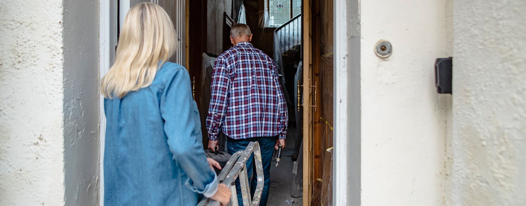 Image of an older man and woman carrying a ladder into a house