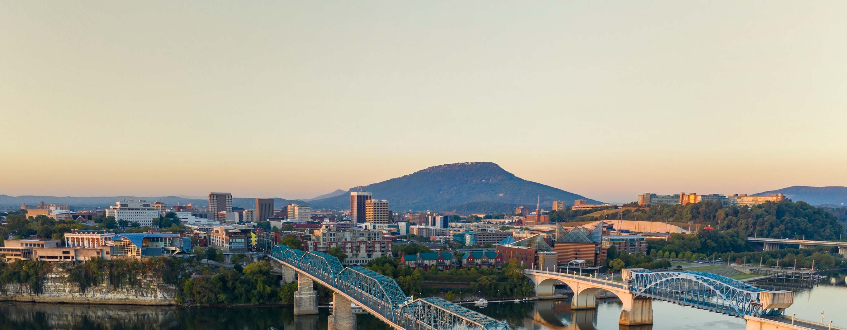 Image of a city skyline with a blue sky, water and mountains nearby