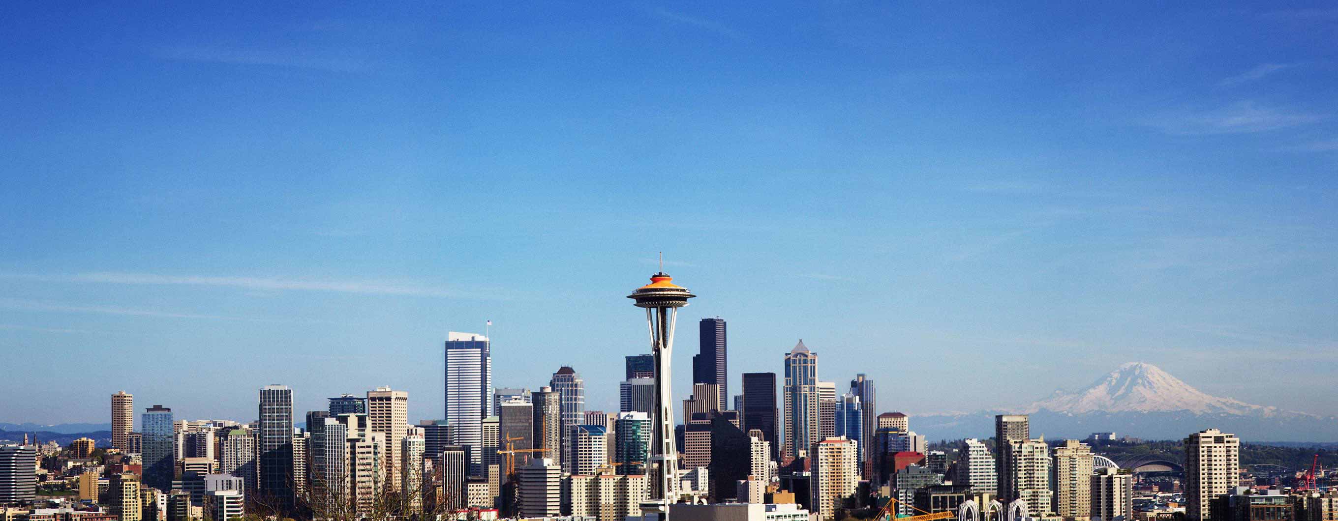 The Seattle skyline in the daytime. There are clouds in the sky. Mount Rainier is visible in the background.