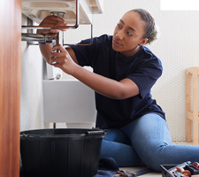 female plumber fixing pipes under the sink
