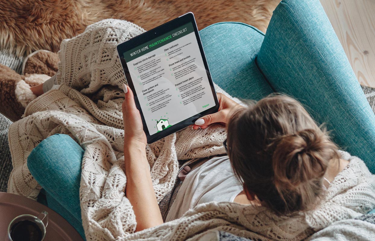 homeowner sitting in their living room, looking at their tablet, and scrolling through a winter home maintenance checklist