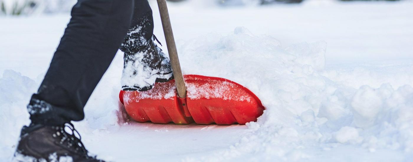 Image of a persons feet and a red shovel shoveling snow