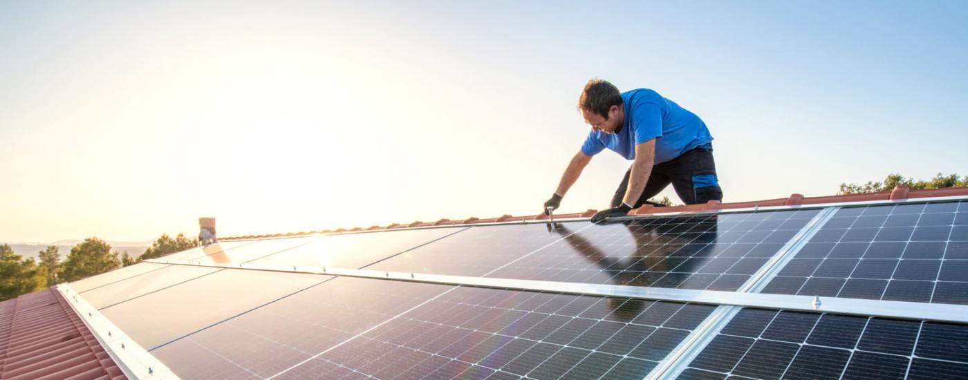 A man works on a solar panel on the roof of a home