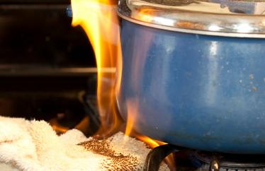 A rag sits on a stovetop under a blue ceramic pot. The rag is on fire.