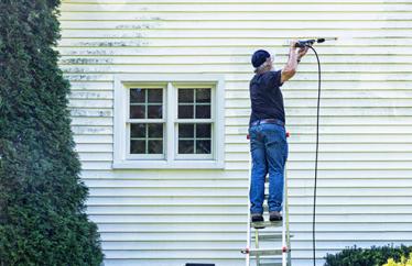 homeowner power washing their home's exterior while standing on a ladder