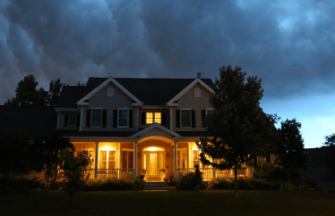 home in the evening with lights on and stormy clouds hovering above it