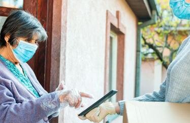 A woman in a mask delivering a package to a senior in a mask.