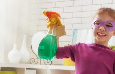 Young girl wearing a superhero mask holds a spray bottle.