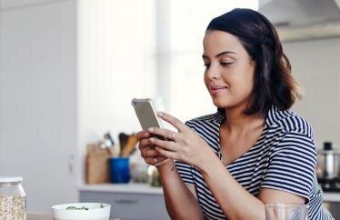 A woman looking at her cell phone in the kitchen