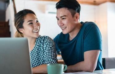 A young couple smiling at each other in front of a laptop
