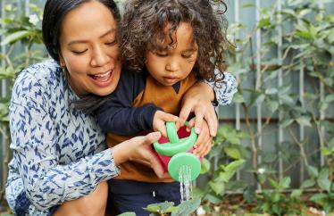 A woman and a young boy watering a plant with a toy watering can