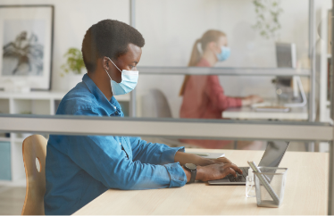 remote worker wearing a mask while they work on their laptop in the office