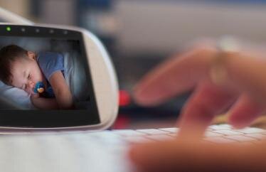 Image of a hand typing on a keyboard with a baby monitor in the background showing a sleeping baby
