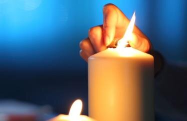 A close up image of a person's hand using a lighter to light a candle in the dark