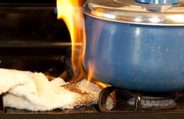 A rag sits on a stovetop under a blue ceramic pot. The rag is on fire. 