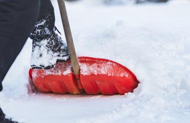 Image of a persons feet and a red shovel shoveling snow