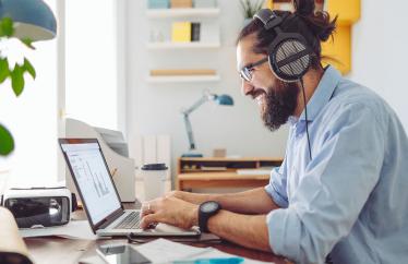 A man works on a laptop at a desk with headphones on