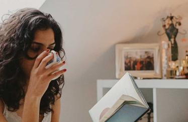 Image of a woman drinking from a mug and reading a book