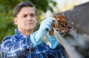 man cleaning leaves out of the gutters in the fall