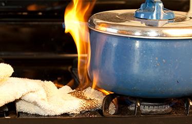 A rag sits on a stovetop under a blue ceramic pot. The rag is on fire.