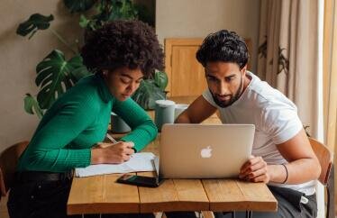 homeowners looking at a laptop and writing down notes to prepare for hail season